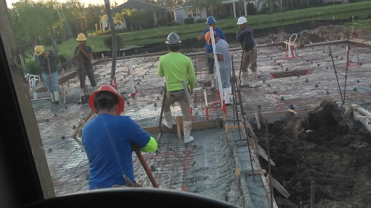 Boom pump line over a freshly placed house slab with crew running power trowels