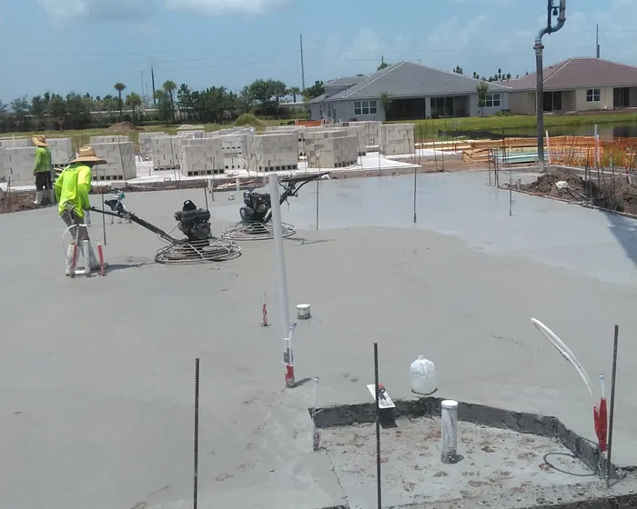 Boom pump line over a freshly placed house slab with two crew running power trowels