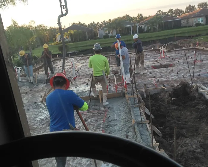 View from inside the pump truck cab of a crew placing and screeding a foundation at dusk