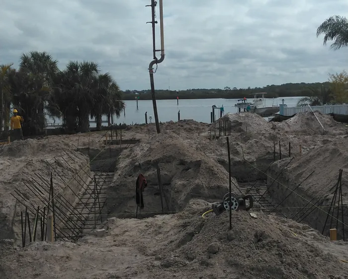 Boom pipe reaching down into excavated footings on a riverfront lot with a dock behind