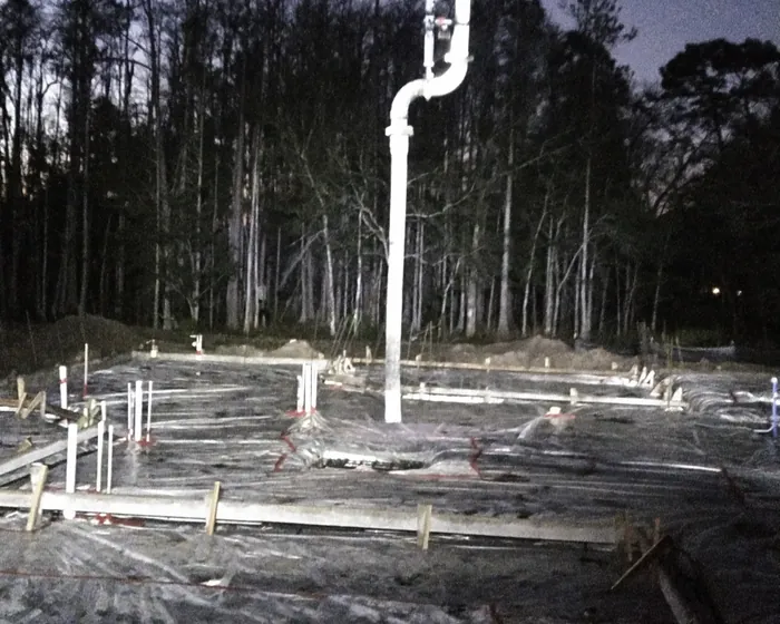 White boom pipe lit up over a formed slab at night surrounded by pine woods